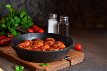 Meatballs in tomato sauce with chilli spices in a pan on a concrete background.