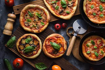 Healthy homemade vegetarian food. Flatlay of rustic freshly baked pizzas with tomatoes, mushrooms, aubergines and basil with pizza knife and raw ingredients on dark background