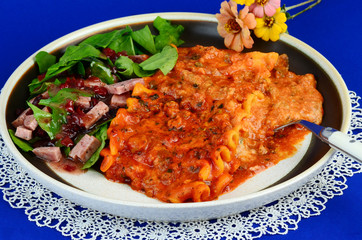 Meat and cheese lasagna with antipasto on white lace doily against blue BG