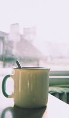 Morning coffee cup with a teaspoon in a kitchen with sunrise and cityscape