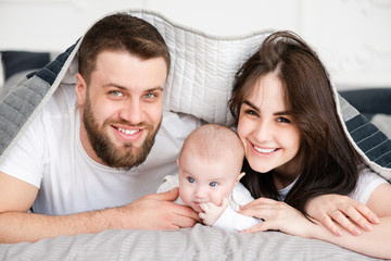Young smiling family with daughter under blanket