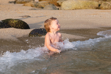 Little boy sitting on the beach in the water