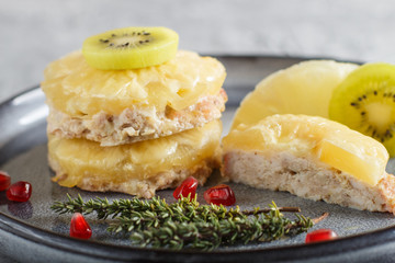 Pieces of baked pork with pineapple, cheese and kiwi on gray plate.