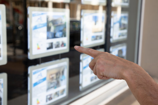 Young Woman Looking Pointing Finger In Window Of Estate Agent