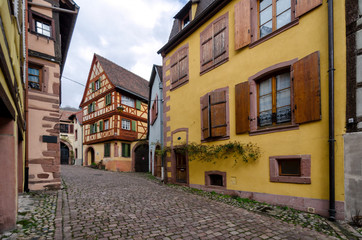 Fototapeta na wymiar View of the street with old half-timbered houses in a small town. Kaysersberg. Alsace. France. In the foreground there is a house of bright yellow color.