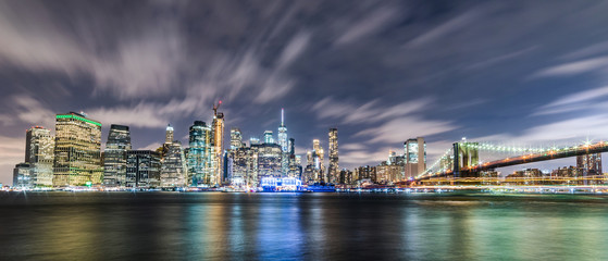 Fototapeta na wymiar Manhattan panoramic skyline at night with Brooklyn Bridge. New York City, USA. Office buildings and skyscrapers at Lower Manhattan (Downtown Manhattan)..