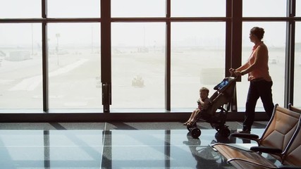 Mother pushes her toddler in a stroller past the big windows
