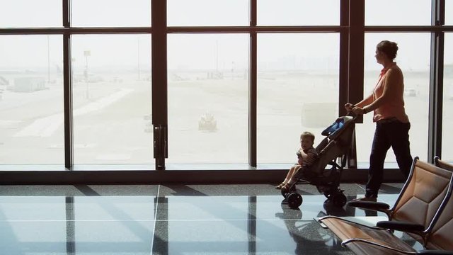 Mother pushes her toddler in a stroller past the big windows