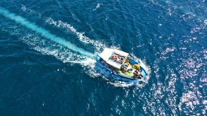 Fototapeta premium Aerial top view photo of traditional fishing boat cruising in Aegean island destination port with deep blue sea