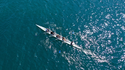 Aerial drone bird's eye view of sport canoe operated by team of young men and women in open ocean sea