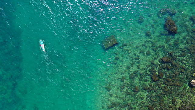 Aerial drone bird's eye view photo of young fit woman practicing paddle board or sup in tropical caribbean sapphire crystal clear calm waters