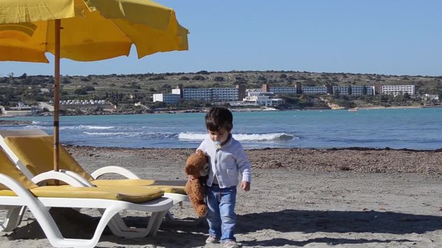 cute two years old boy with teedy bear on the sandy beach colder weather