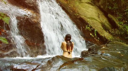A woman bathes in the forest waterfall