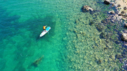Aerial drone bird's eye view photo of young fit woman practicing paddle board or sup in tropical caribbean sapphire crystal clear calm waters