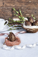Handmade chocolate Easter eggs on a table decorated with satin ribbons, green branches and a Cup of coffee and a wooden background.