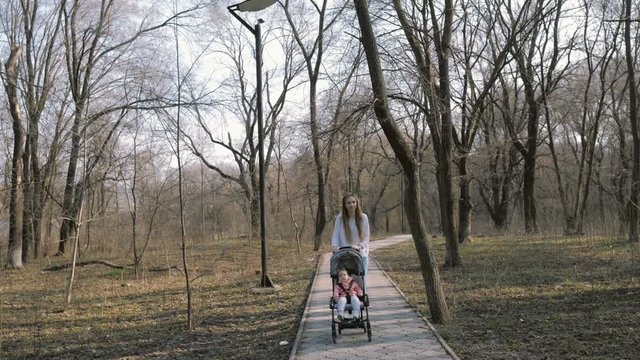 Young mother walking with a baby girl in stroller in the park