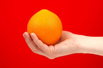 Ripe juicy delicious orange in hand isolated on red background. Healthy eating and dieting concept