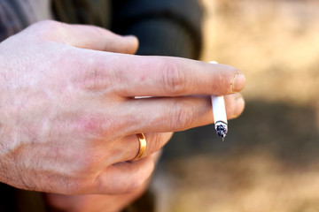 Cigarette in the brutal male man hand with wedding ring. Smoking is a bad habit
