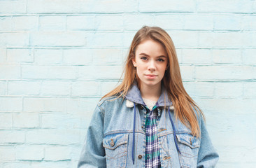 Portrait of a beautiful blonde girl on a blue background, looking into the camera with a serious...