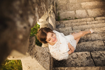 Young woman in white dress sitting near the old wall of castle
