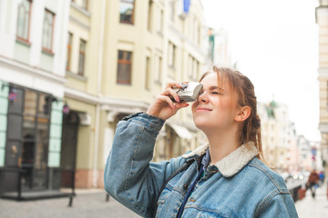Portrait of a tourist girl takes a photo of architecture on a retro film camera, wearing a denim...
