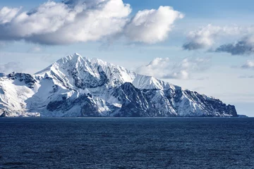 Fotobehang Snow peaks, glaciers and rocks of Aleutian islands in sunny winter day as viewed from ship passing in calm sea © Oleksii Fadieiev