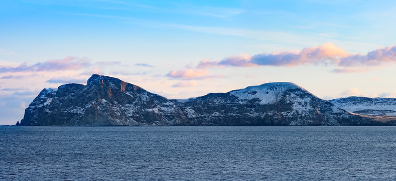 Snow peaks, glaciers and rocks of Aleutian islands in sunny winter day as viewed from ship passing in calm sea