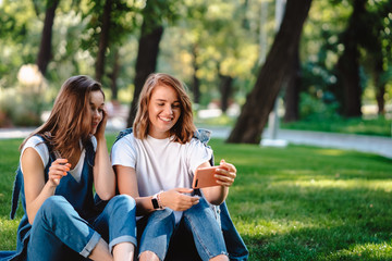 Two female friend holding mobile phone while sitting on a grass