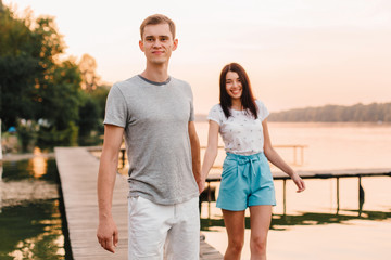 Loving young couple walking on pier at sunset in summer.