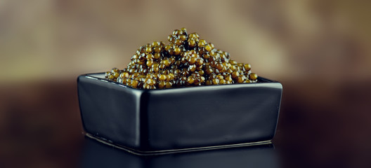 Black Caviar closeup. Natural sturgeon black caviar in square dish on black background. Delicatessen