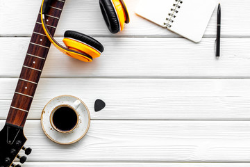 Musician work place with guitar, earphones, notebook and coffee on white wooden background top view...