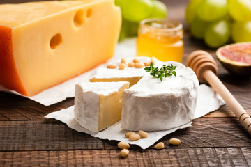 Brie or Camembert cheese, slice of yellow cheese, honey, grapes and figs on a wooden table background
