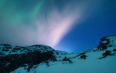 Naklejka premium Aurora borealis above the snow covered mountain range in europe. Northern lights in winter. Night landscape with green polar lights and snowy mountains. Starry sky with aurora. Nature. Space