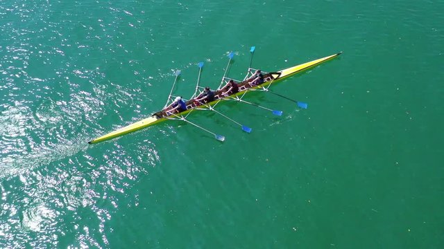 Aerial drone bird's eye view video of yellow sport canoe operated by team of young team in emerald clear sea