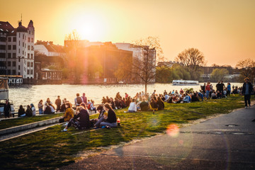 Menschen genießen den Sonnenuntergang am Fluss neben der Berliner Mauer / East Side Gallery in Berlin, Deutschland