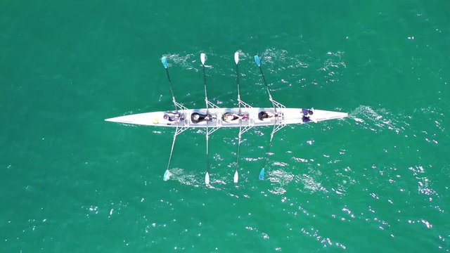 Aerial drone bird's eye view video of red sport canoe operated by team of young men and women in emerald clear sea