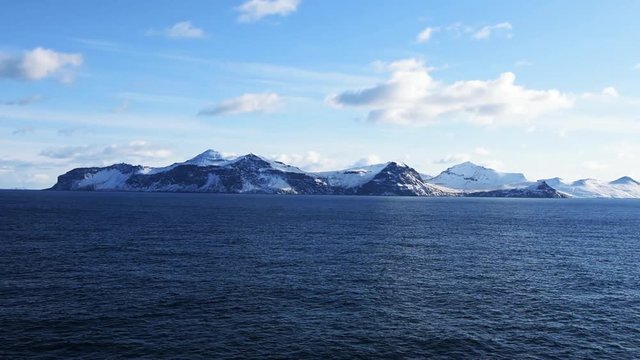 Snow peaks, glaciers and rocks of Aleutian islands in sunny winter day as viewed from ship passing in calm sea