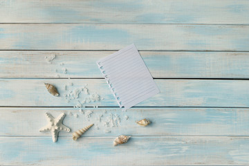Seashells, sea salt and star on blue wooden background and sheet of paper as a vacation concept with copy space