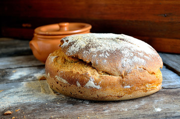 Homemade rustic bread, clay pot on a wooden background.