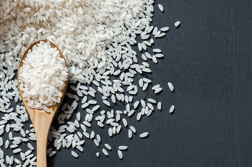 turkish raw white rice grains in wooden spoon on black wooden background, healthy food uncooked legumes concept