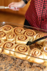 Woman Lifting Home Made Cinnamon Roll From a Glass Baking Dish