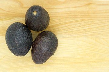 Fototapeta na wymiar three riper avocados on a light brown table