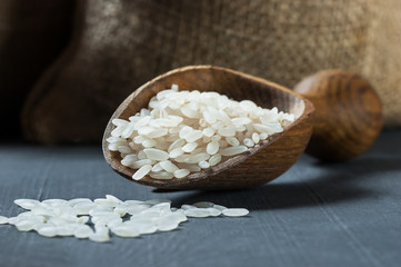 turkish raw white rice grains with burlap sack in wooden shovel on black wooden background, healthy food uncooked legumes concept