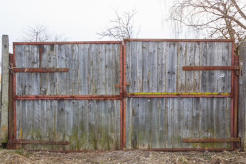 Old gray gate on large rusty hinges