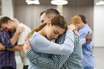 Waist up portrait of people hugging during group therapy session, focus on smiling young woman in...