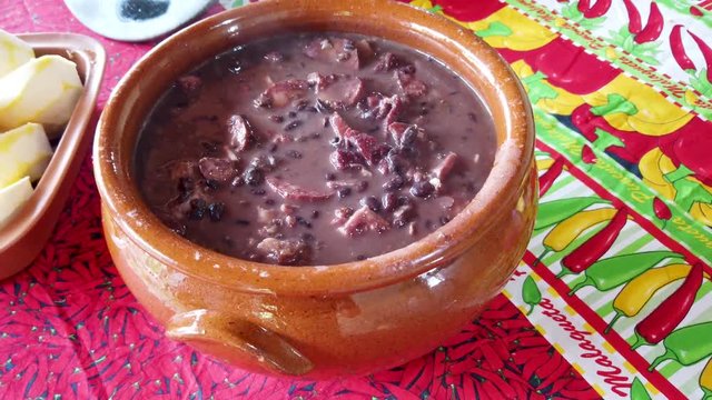 Tradicional brazilian feijoada pan served in a clay pot with smoke, movement  close up