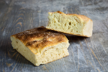 Italian bread of Focaccia Genovese type on a rustic wooden table, sliced in two squared pieces. The focaccia is a traditional oven baked flat bread, this one coming from Genoa, or Genova
