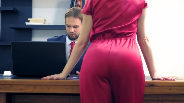 Office flirt. Attractive woman in a red jumpsuit, flirting at the table with her colleague.