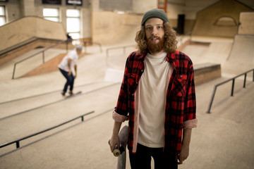 Portrait of long haired skater standing in extreme sports park and looking at camera , copy space