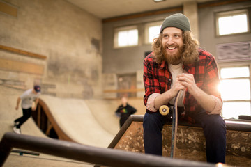 Portrait of long haired skater sitting on ramp in extreme park and smiling, copy space © Seventyfour